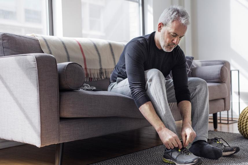 A man sitting on a couch and tying his shoelace